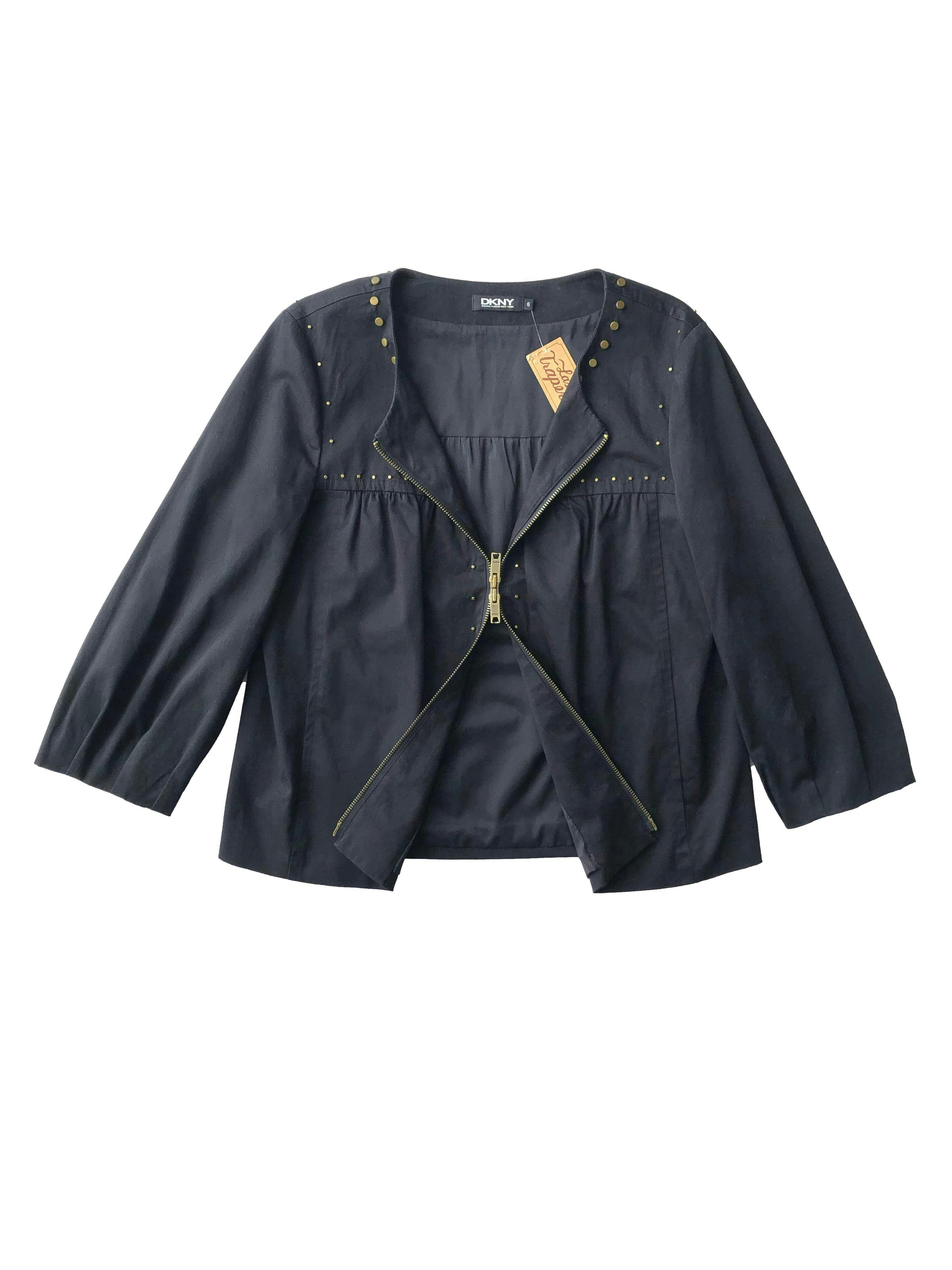 Casaca negra DKNY de drill 97% algodón con tachas bronce, forro, recogido en pecho, mangas abullonadas, bolsillos y cierre doble sentido. Busto 108cm, Largo 56cm.