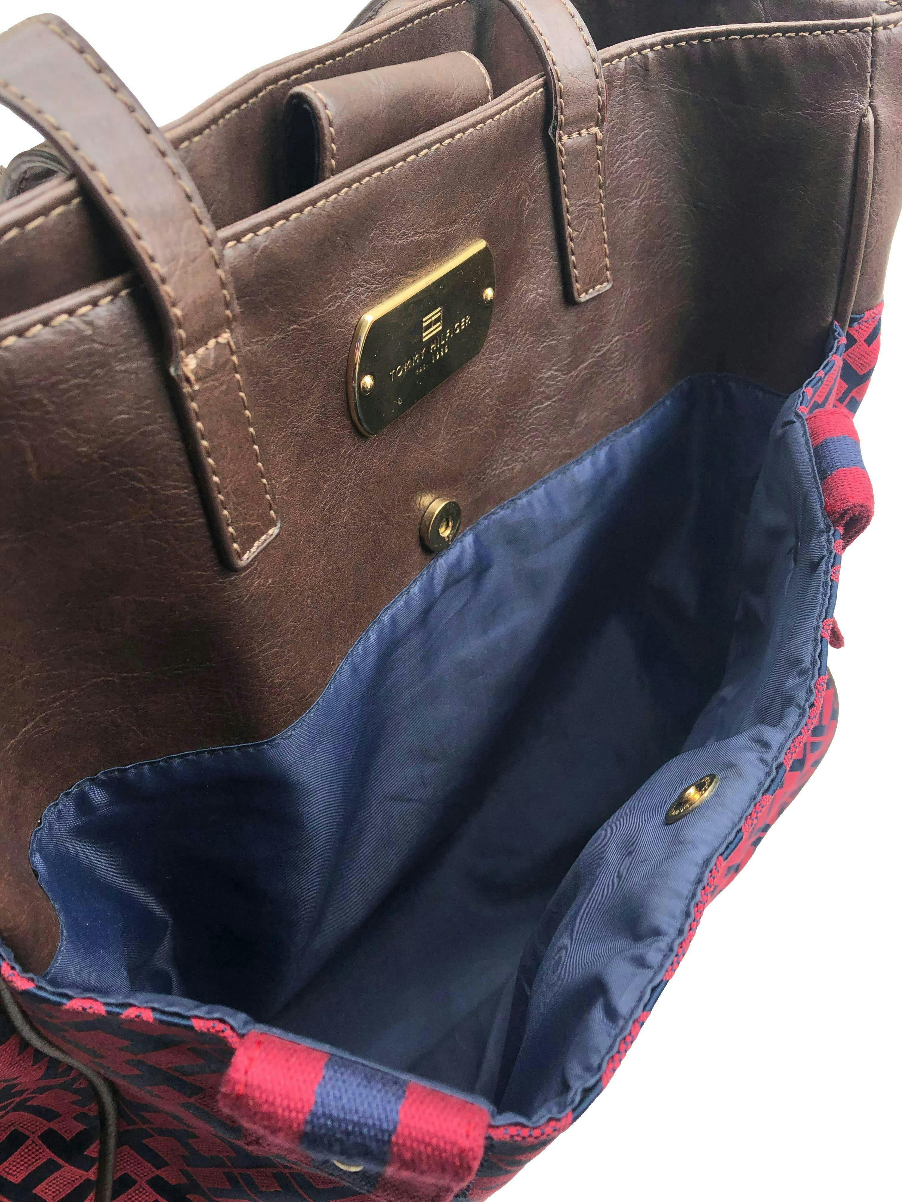 Cartera Tommy Hilfiger monograma azul y rojo con detalles tipo cuero marrón, forro interno con un compartimento con zipper, cierra co broche. Medidas 34x33x12cm.  Nueva