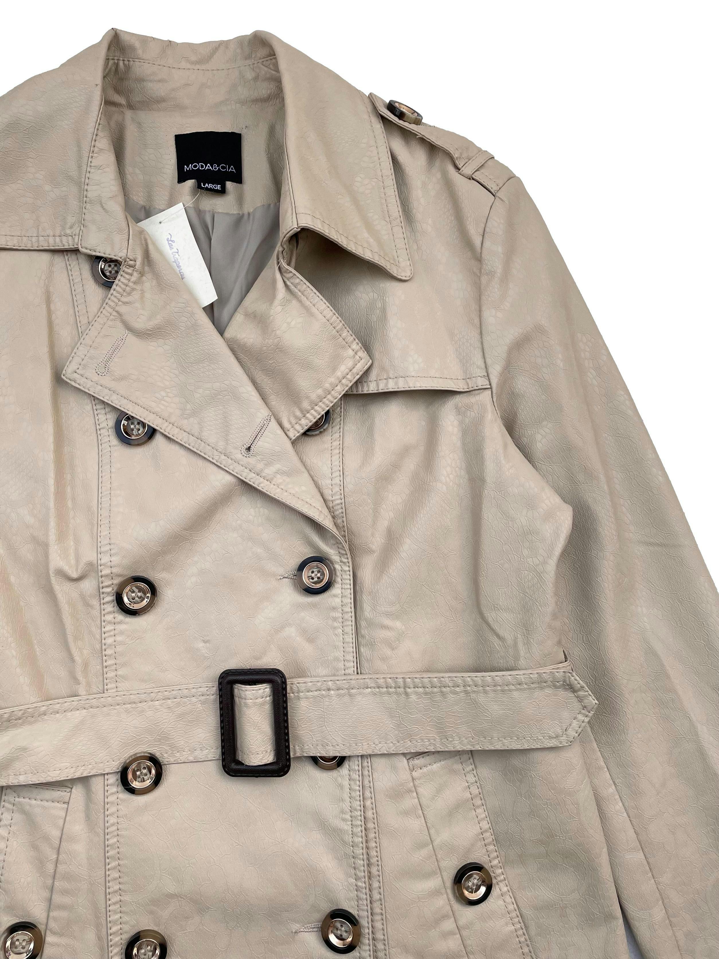 Trench Coat Moda&Cia de cuerina beige texturizada, forrada, dos bolsillos, cinturón y botón de repuesto. Busto 104cm Largo 66cm. Precio original S/450