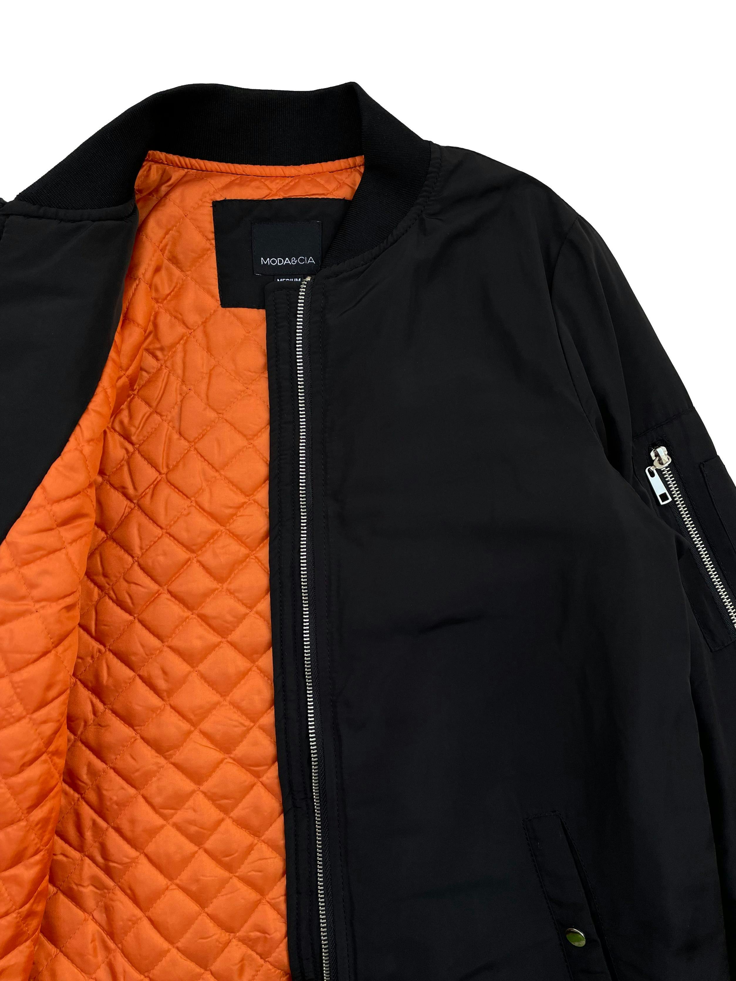 Bomber jacket Moda&Cia negra con forro naranja, ligeramente acolchada, cierre frontal , dos bolsillos delanteros y un bolsillo con cierre en el brazo. Busto 102cm , Largo 75cm. Precio original S/ 399