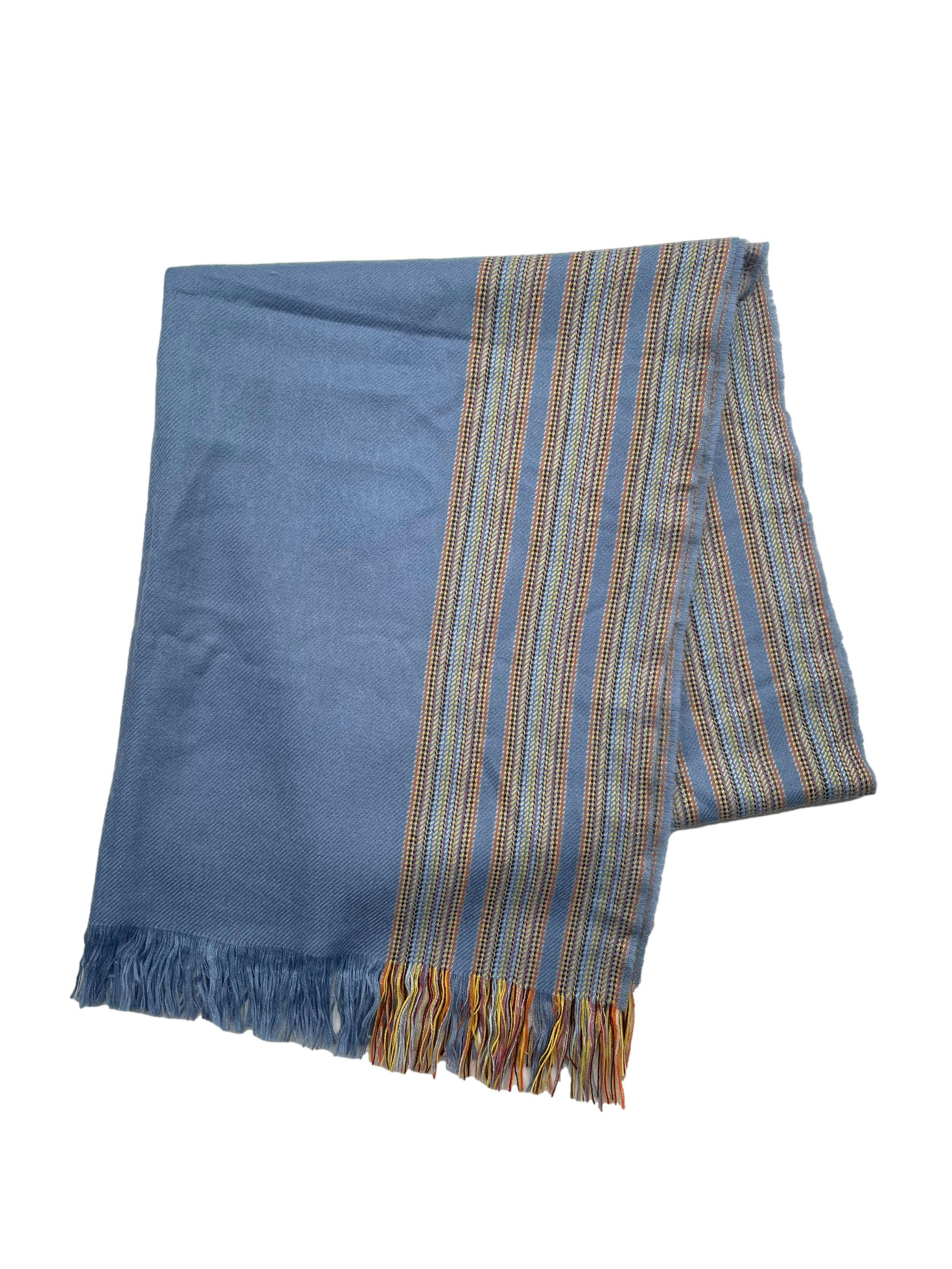 Bufanda tipo chal gris azulado con lineas en tonos cálidos y bordes desflecados. Medidas 72x 170cm.